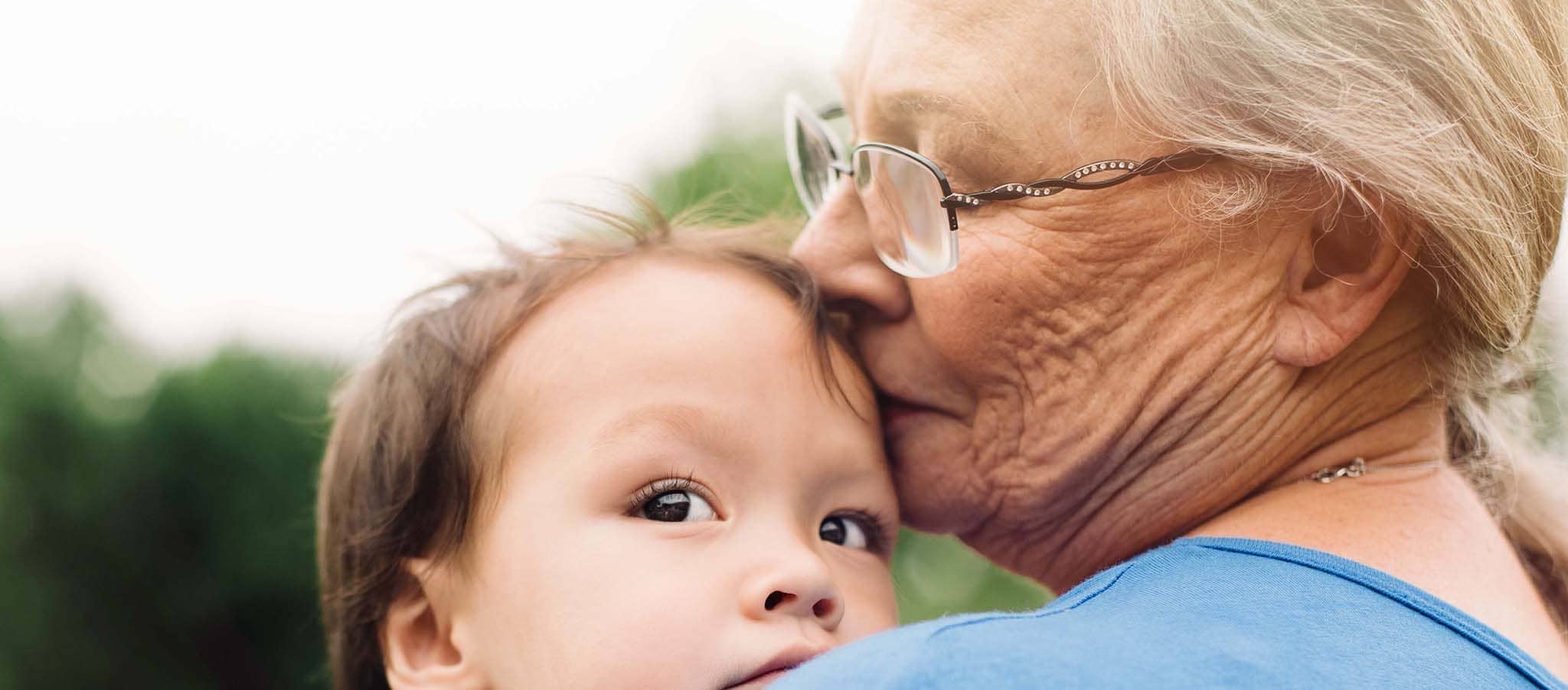 Woman in blue shirt holding a baby and kissing him on the forehead